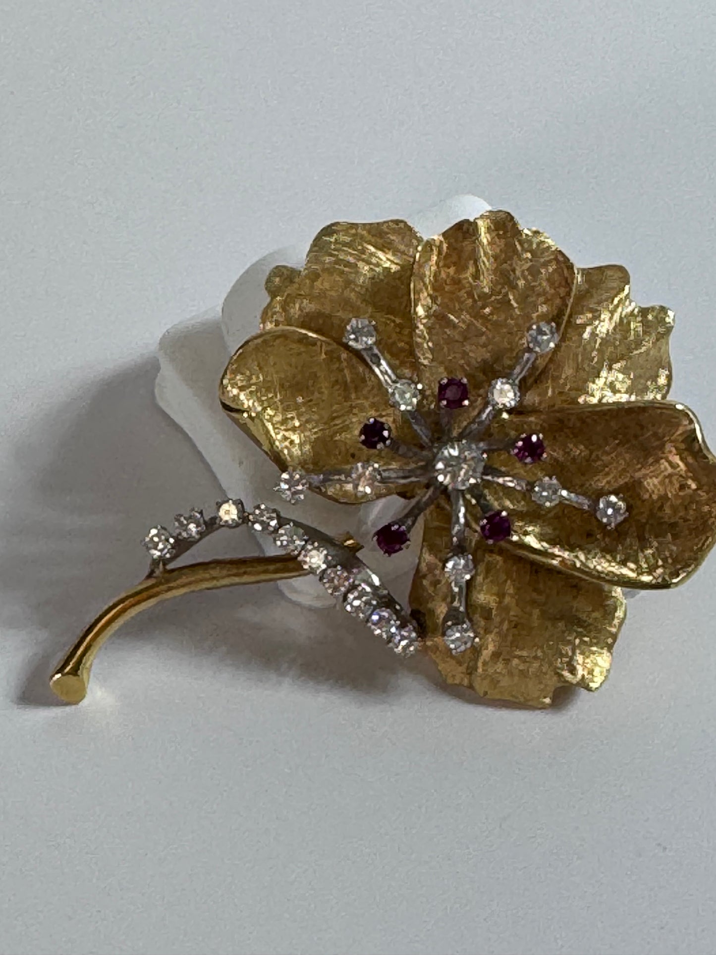 Gold flower-shaped brooch with gemstones on a white background
