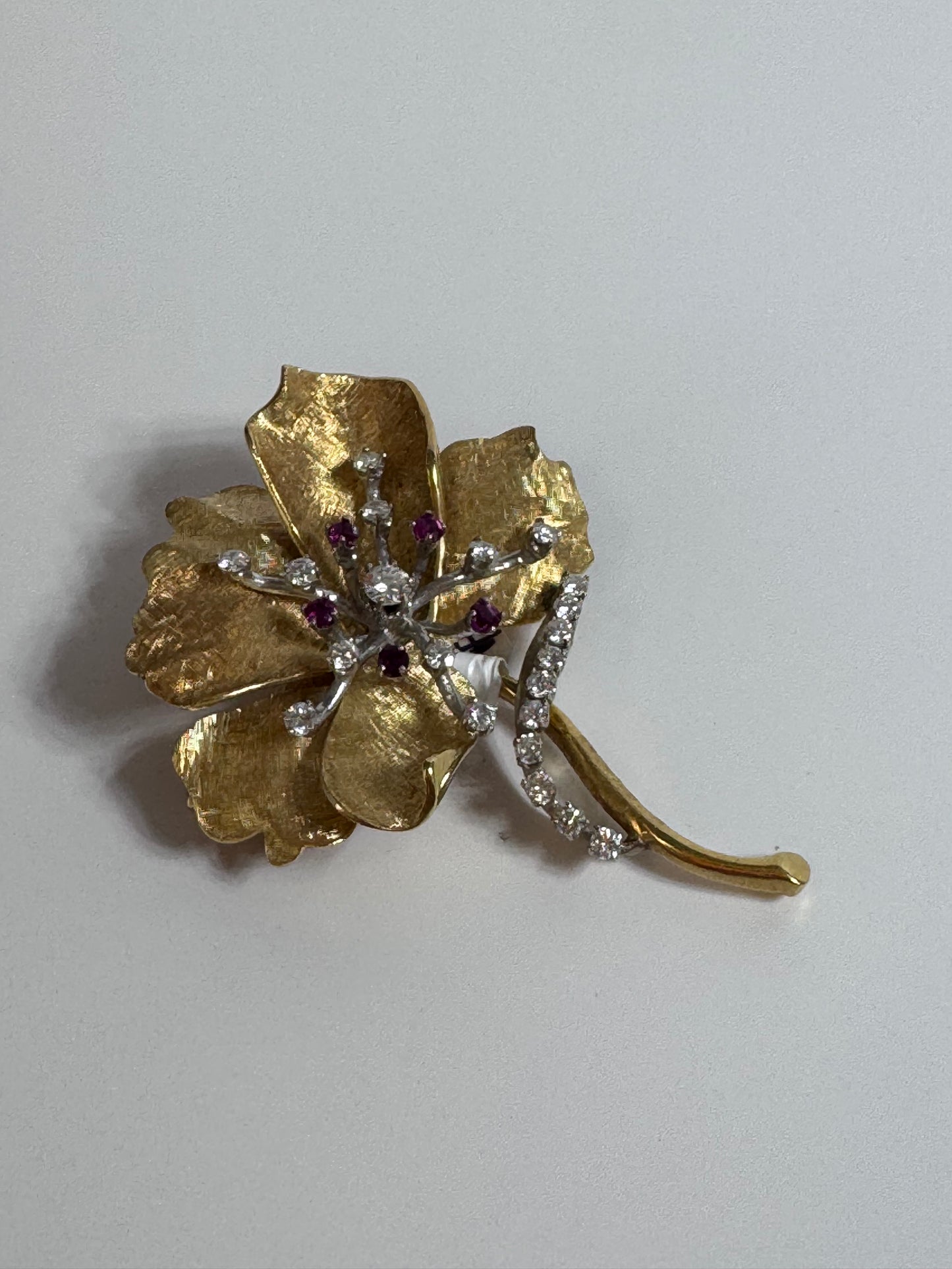 Gold flower-shaped brooch with gemstones on a white background
