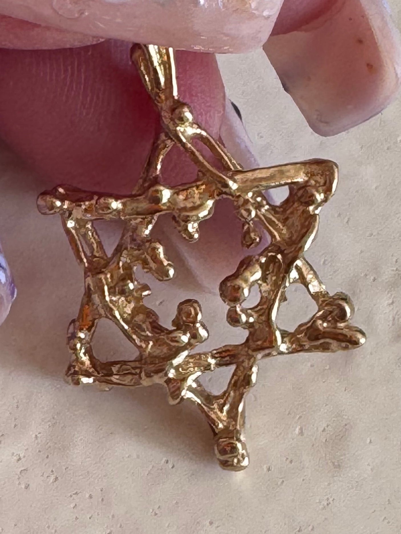 Gold star-shaped brooch held by a hand on a beige background