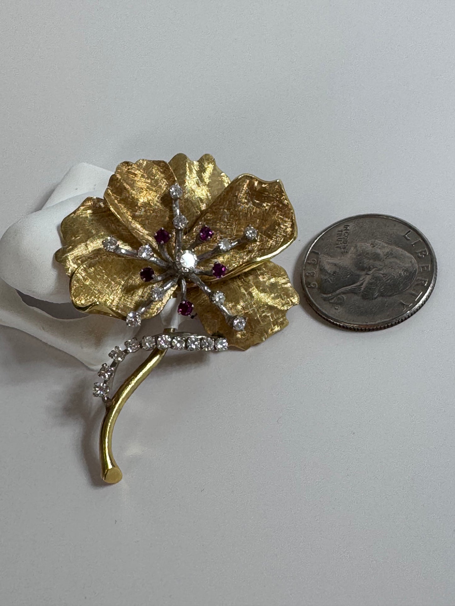 Gold flower-shaped brooch with gemstones on a white background, next to a quarter for scale.