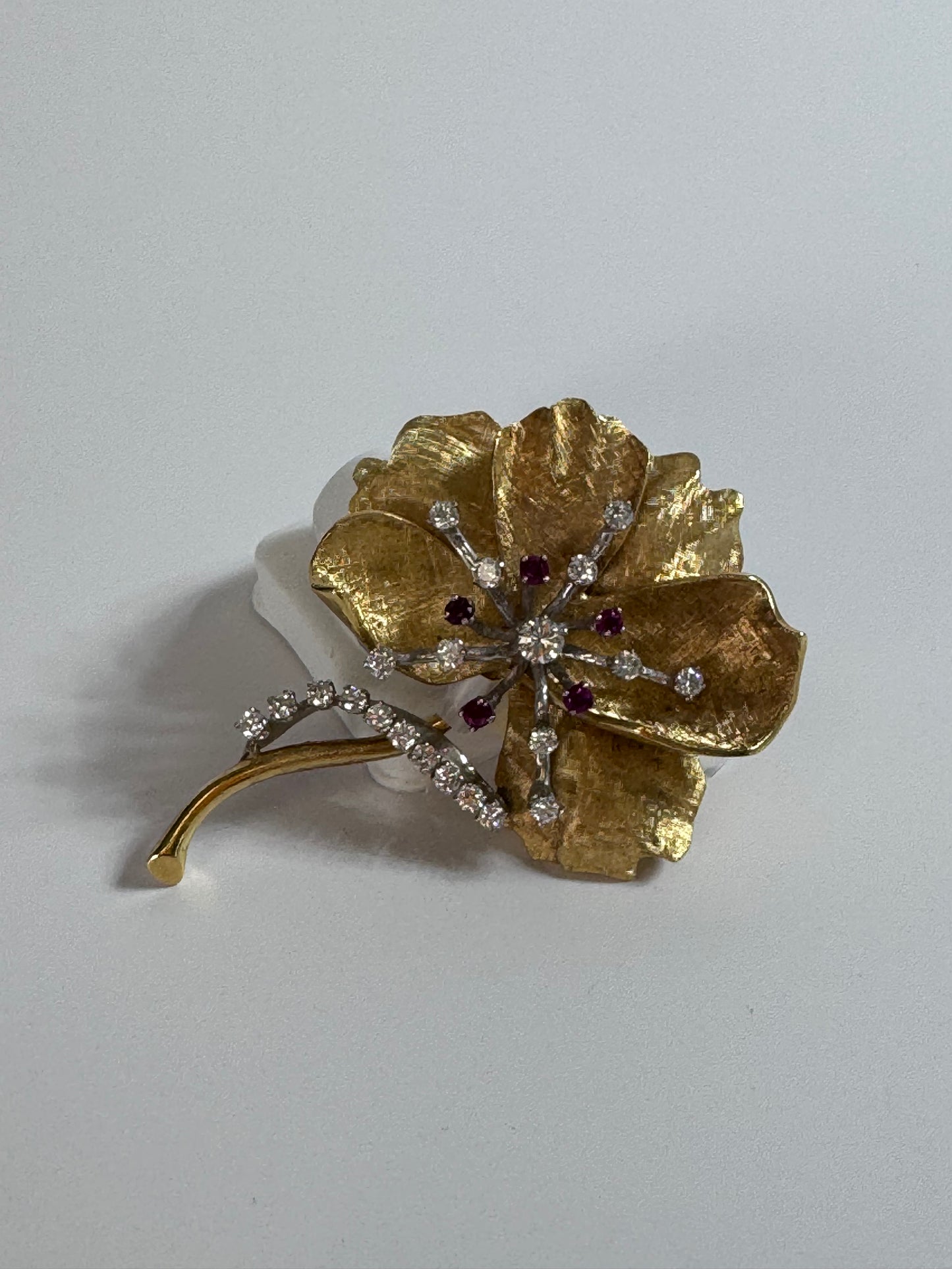 Gold flower-shaped brooch with gemstones on a light gray background