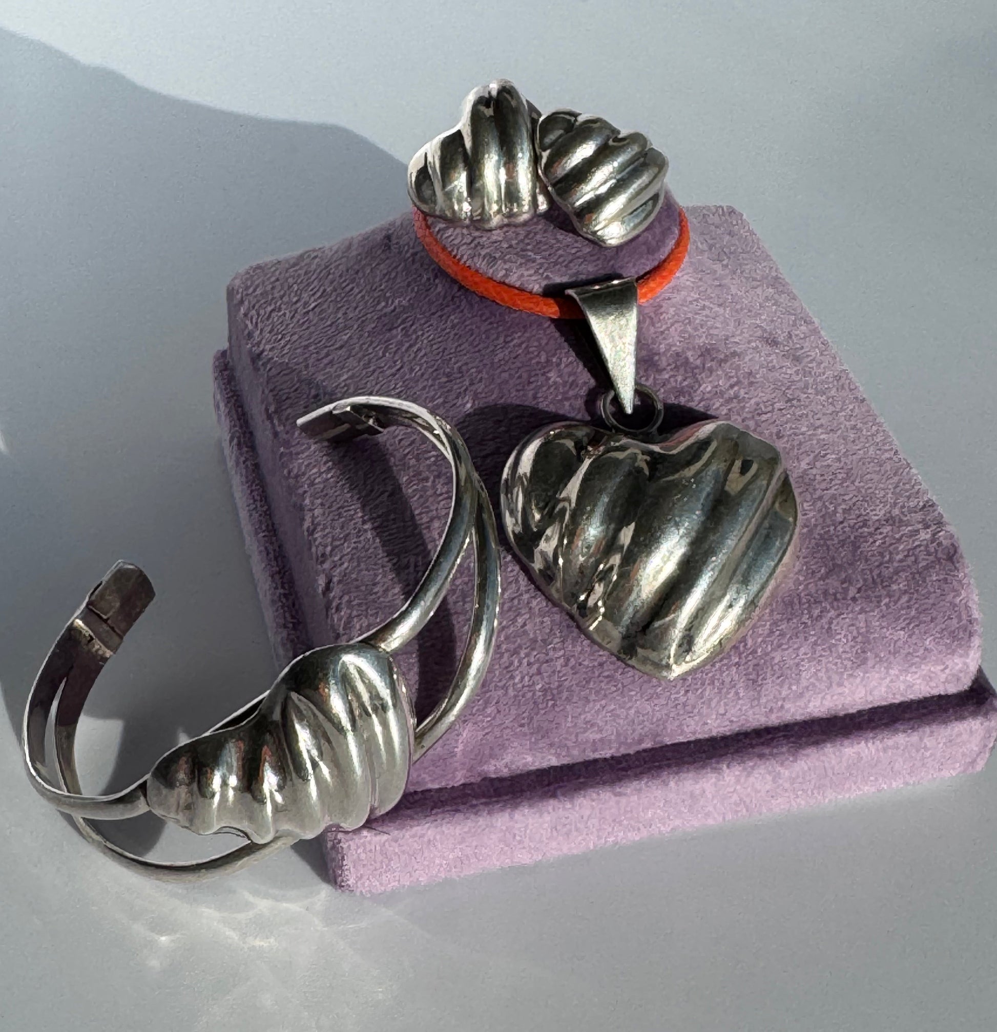 Sterling silver puffy heart jewelry set including cuff bracelet, stud earrings, and pendant with orange cord