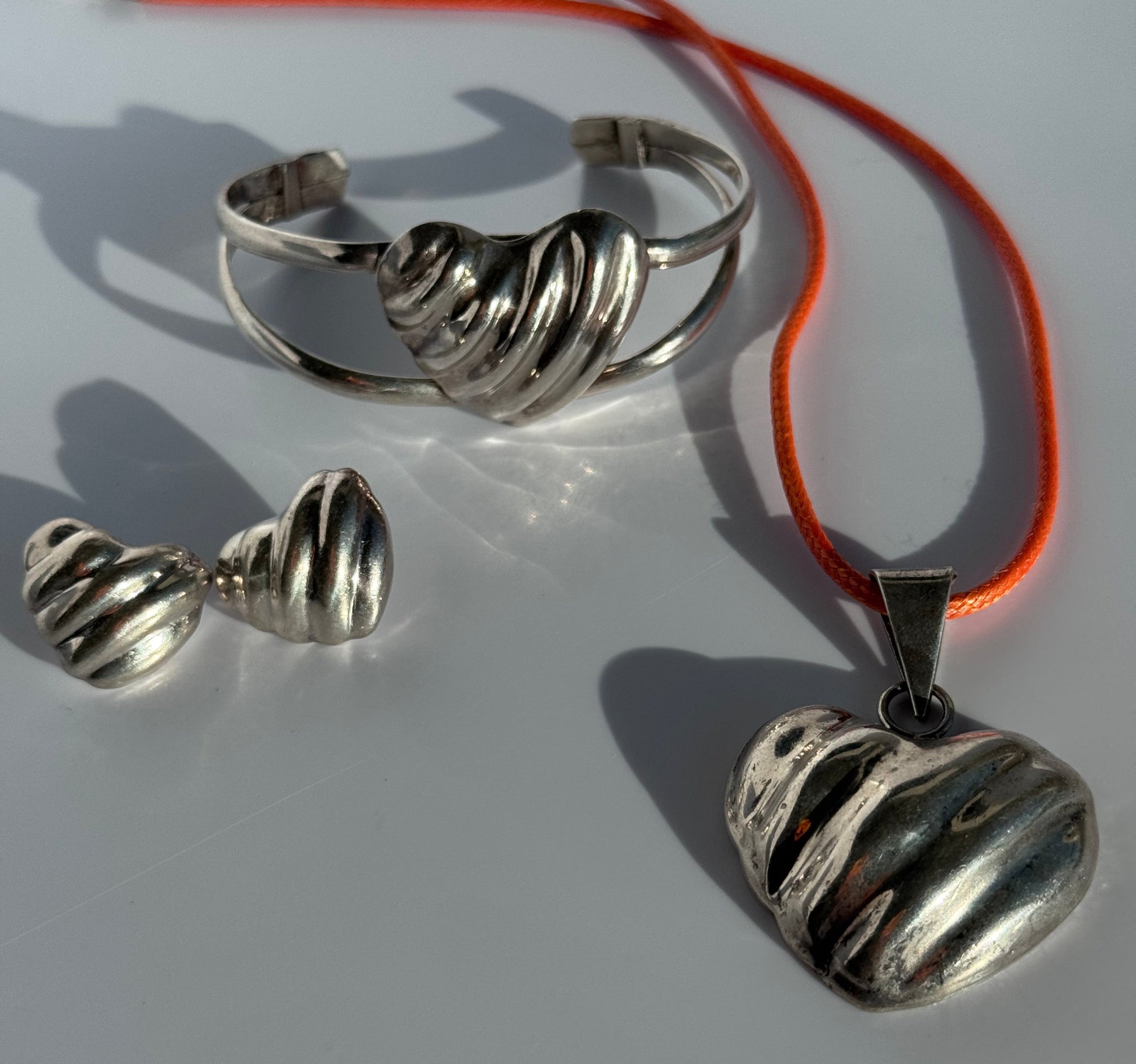 Sterling silver puffy heart jewelry set including cuff bracelet, stud earrings, and pendant with orange cord