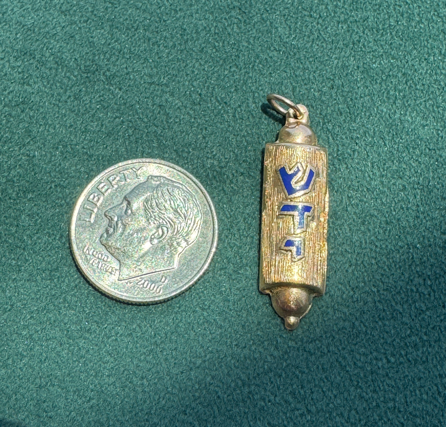 Small cylindrical metal object with blue and gold design next to a U.S. dime on a green textured surface