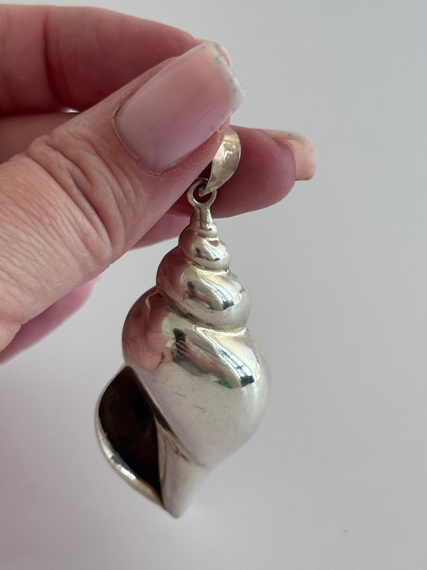 Large vintage sterling silver conch shell pendant with AI signature, showing detailed spiral shell design and high-polish finish