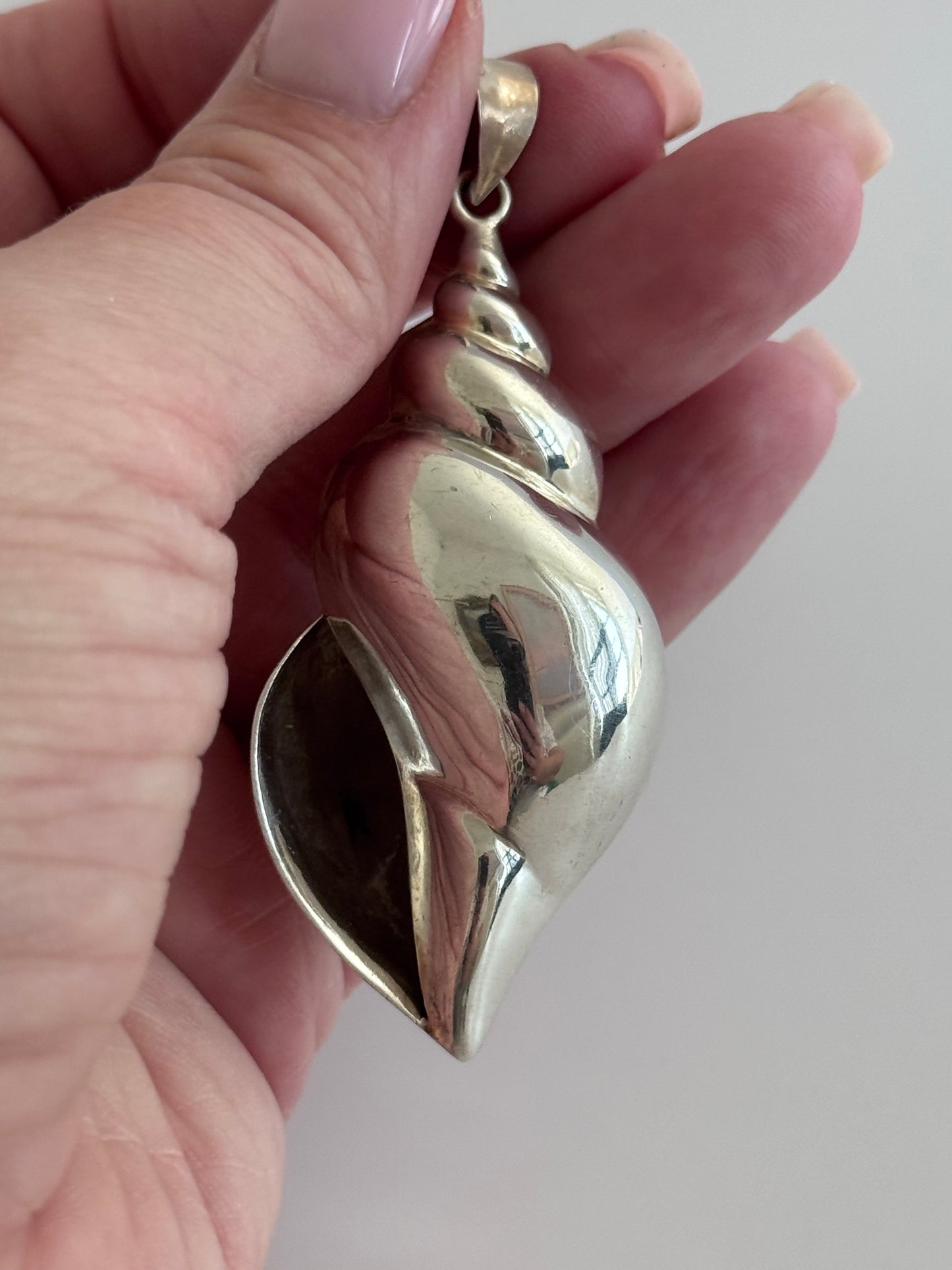 Large vintage sterling silver conch shell pendant with AI signature, showing detailed spiral shell design and high-polish finish