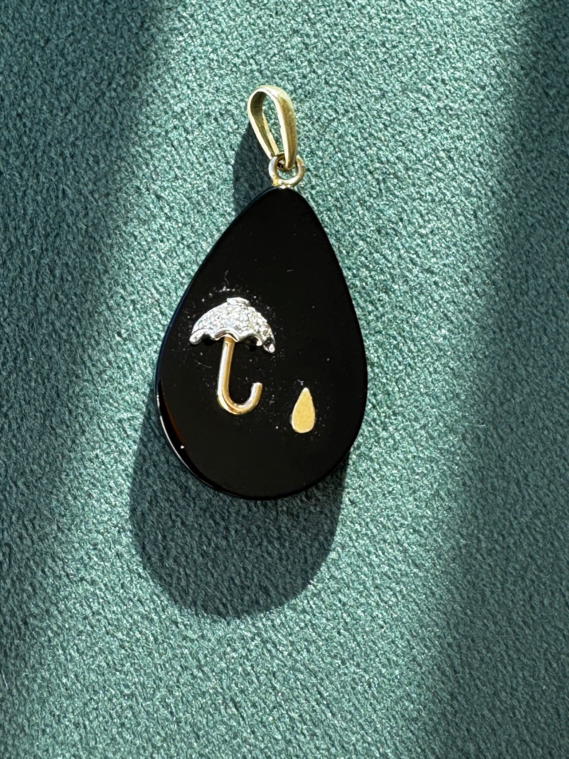 Black teardrop-shaped pendant with gold accents on a green textured surface