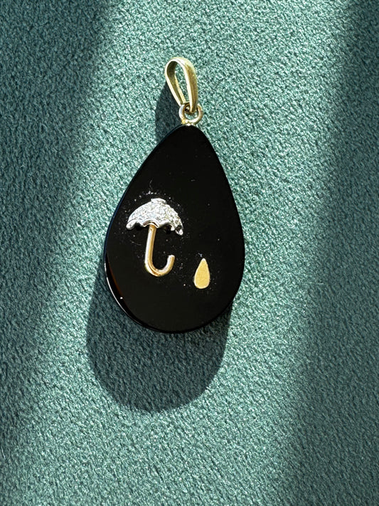 Black teardrop-shaped pendant with gold accents on a green textured surface