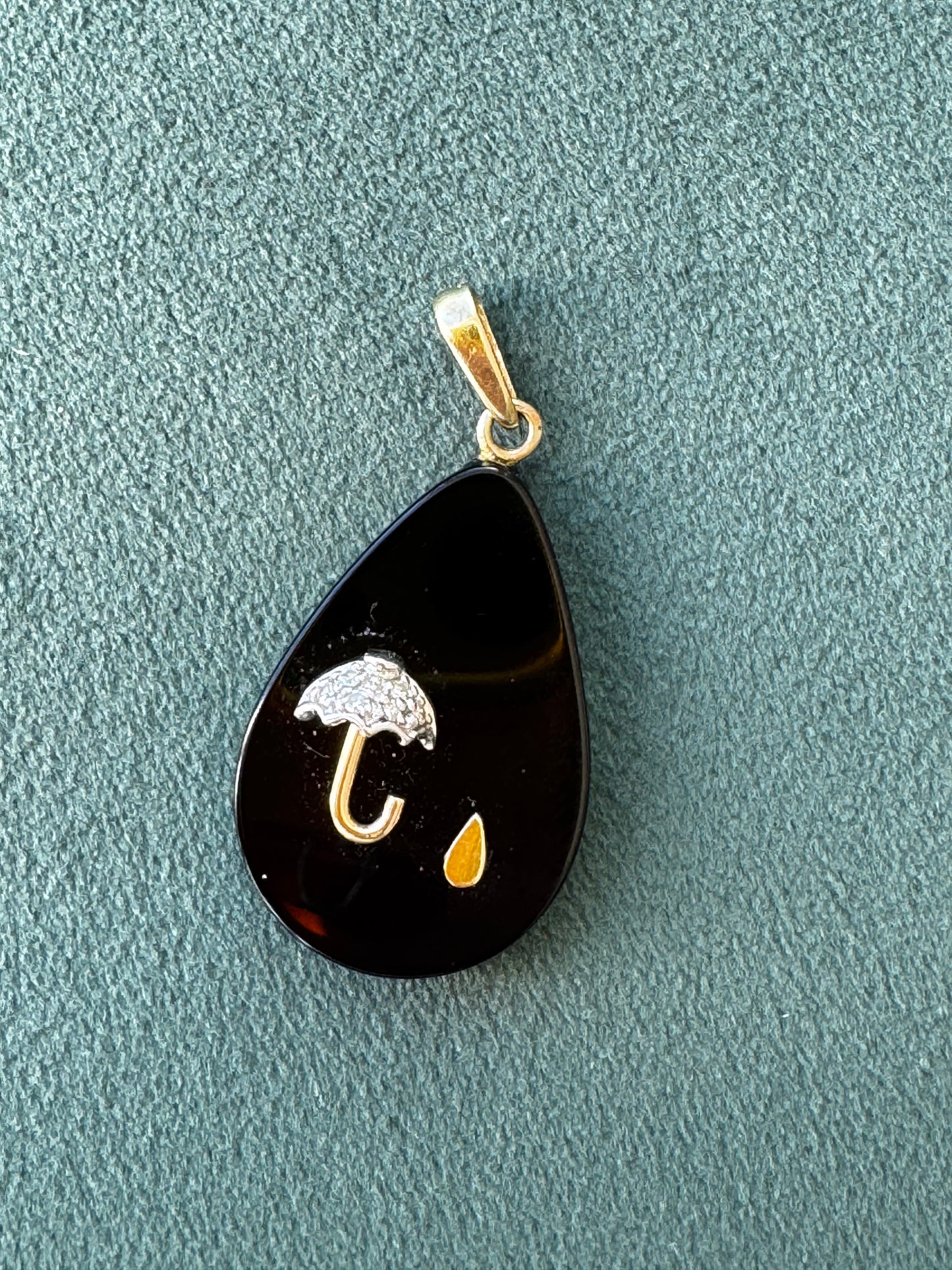 Black teardrop-shaped pendant with gold and white accents on a textured gray surface