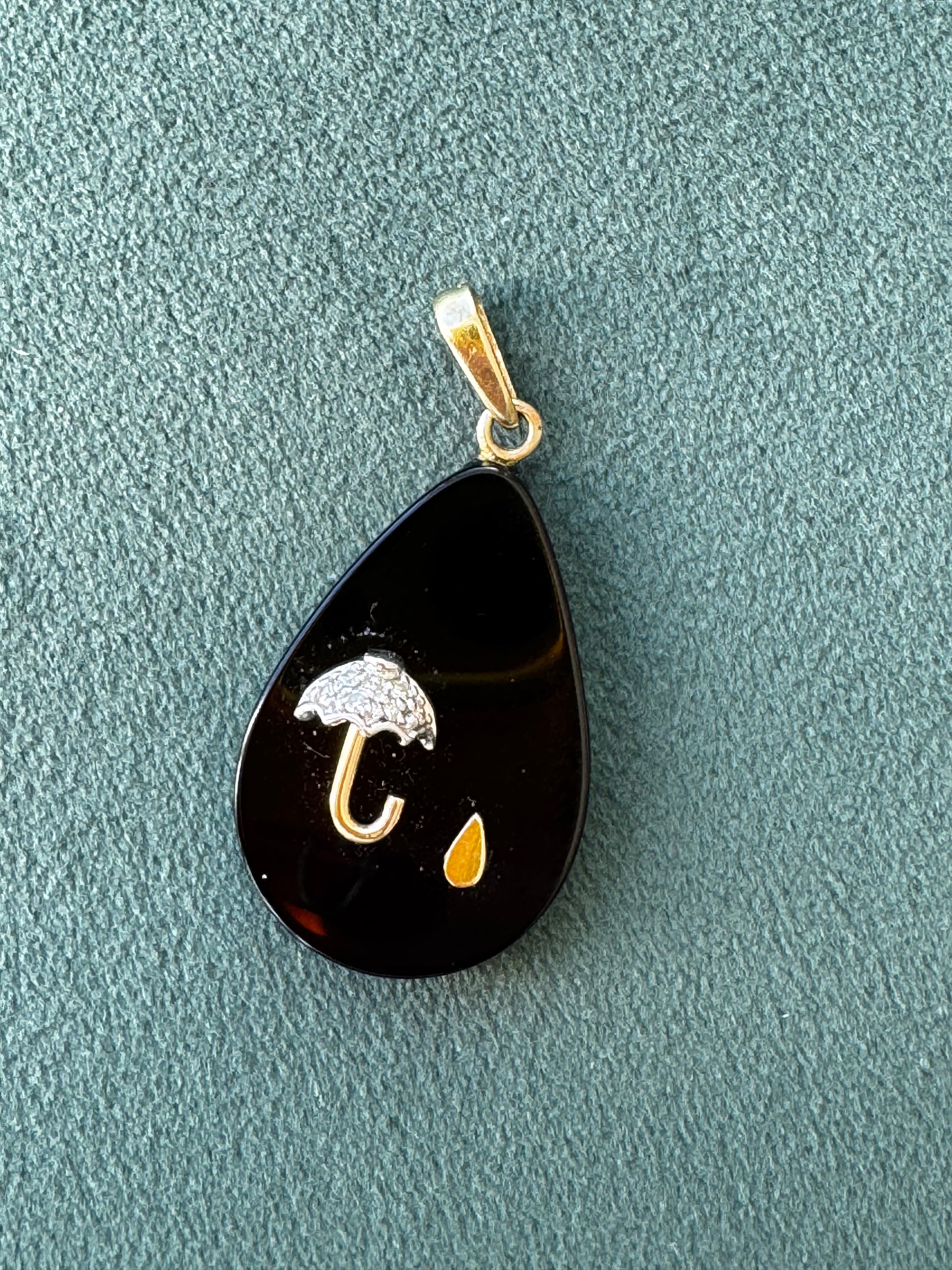 Black teardrop-shaped pendant with gold and white accents on a textured gray surface