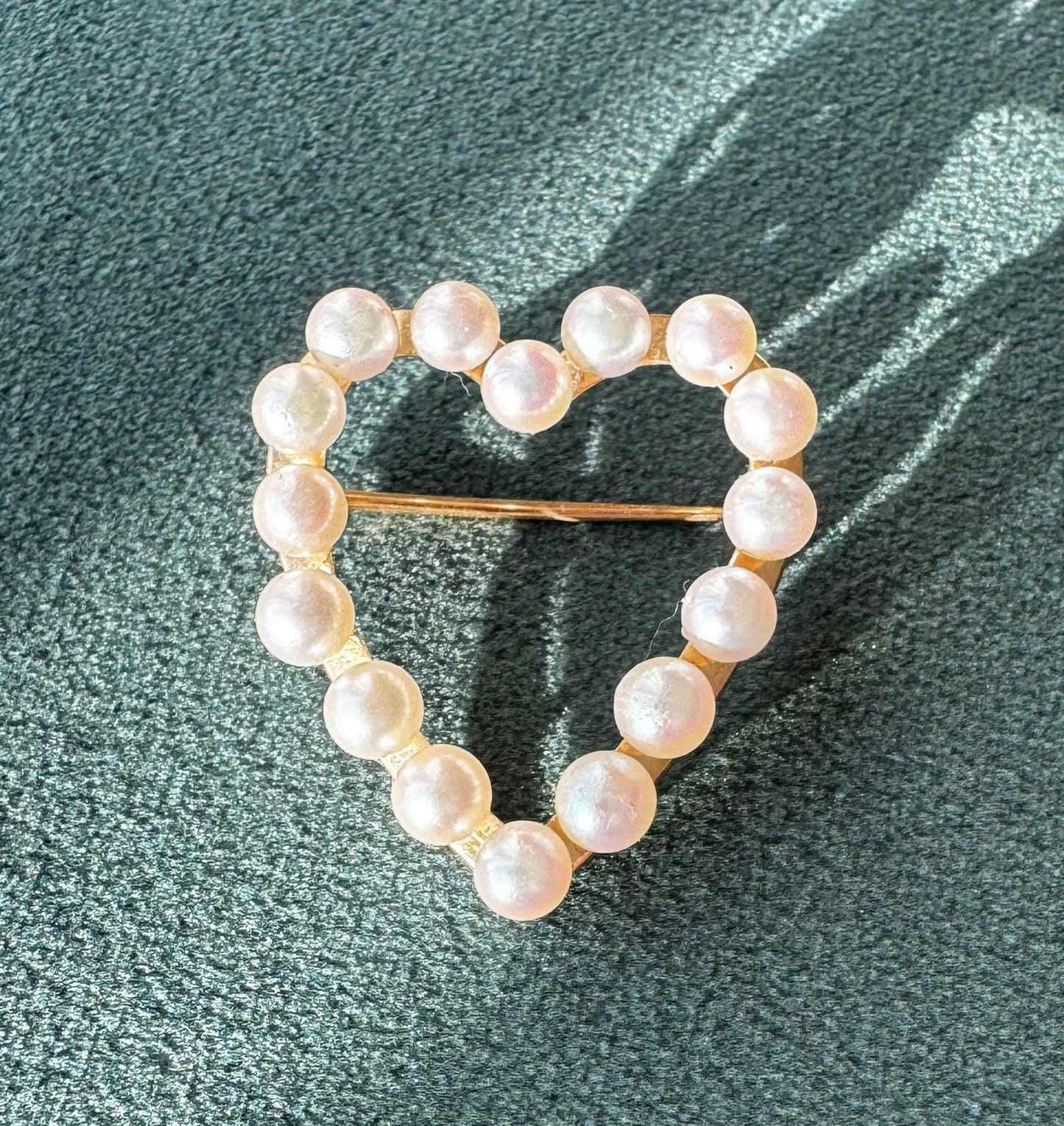 Pearl heart-shaped brooch on a textured green surface