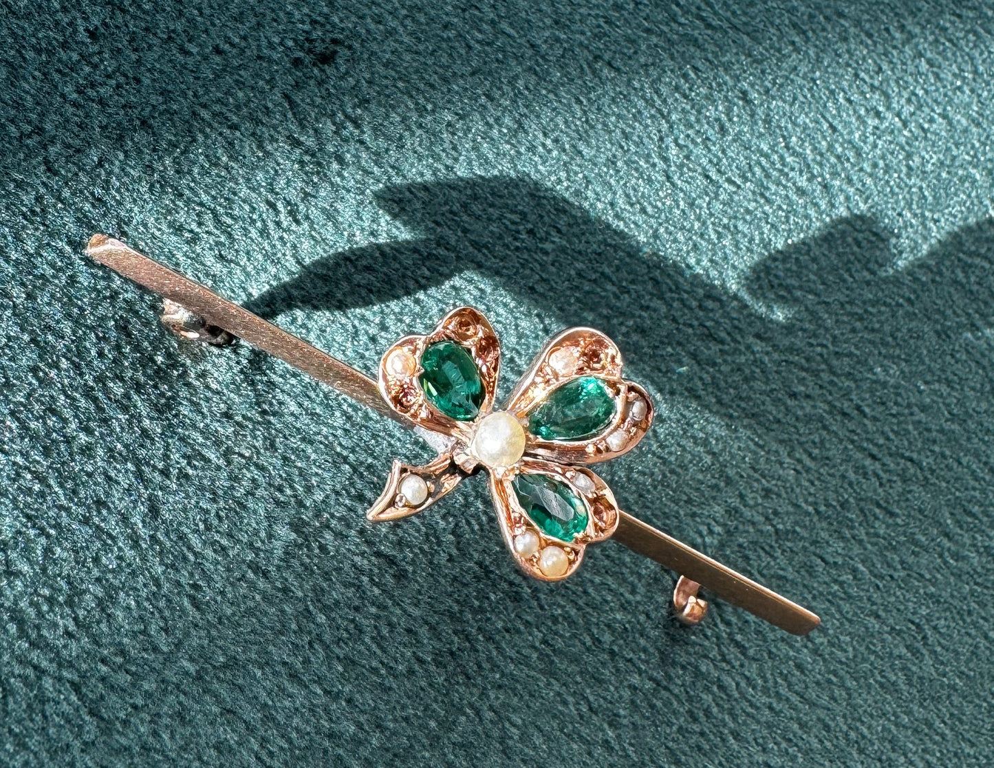 Gold brooch with green gemstones on a textured teal surface
