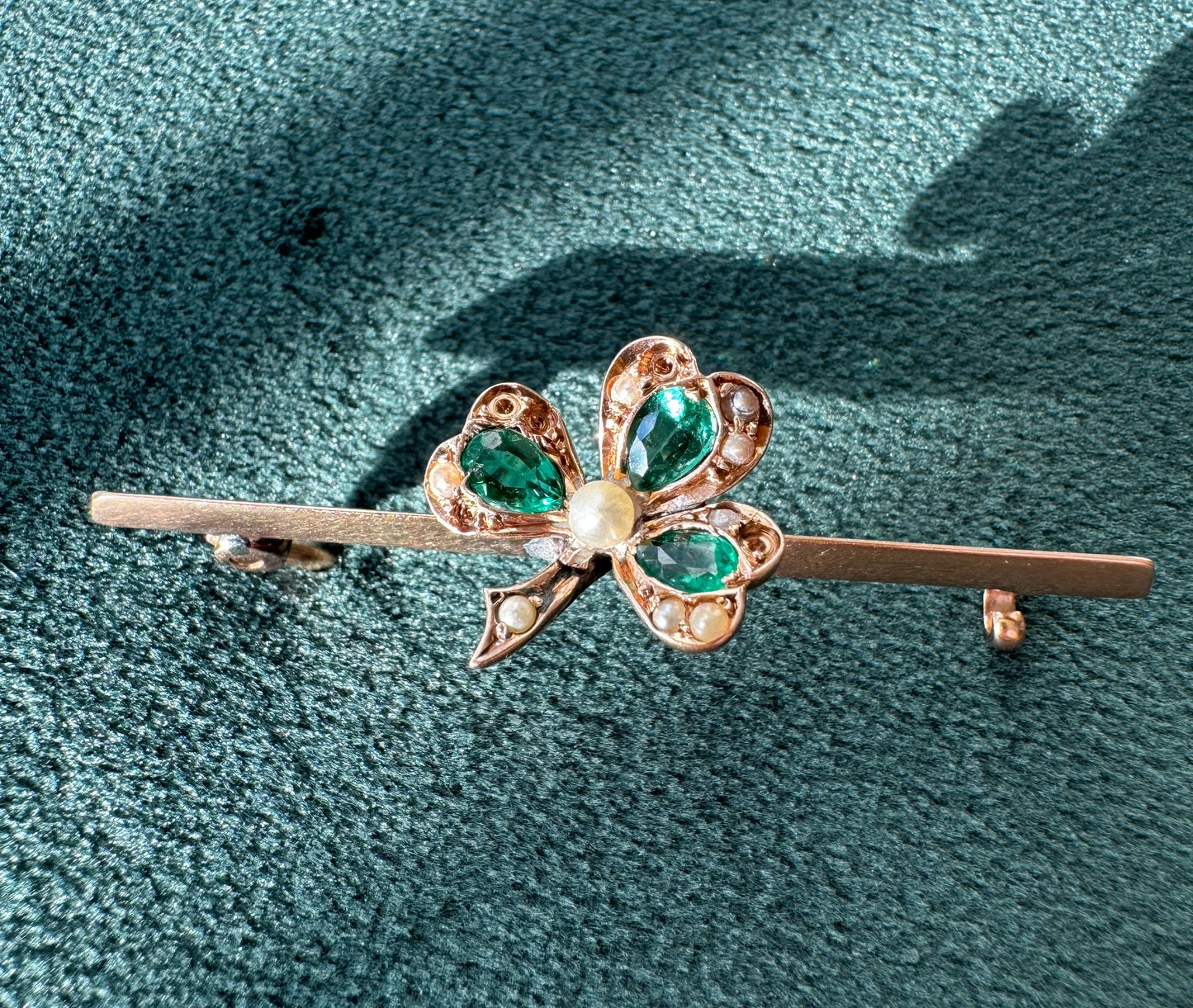 Gold brooch with green gemstones on a textured green background