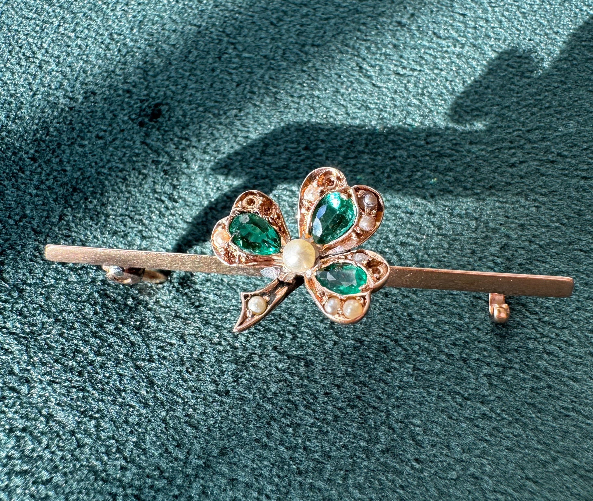 Gold brooch with green gemstones on a textured green background
