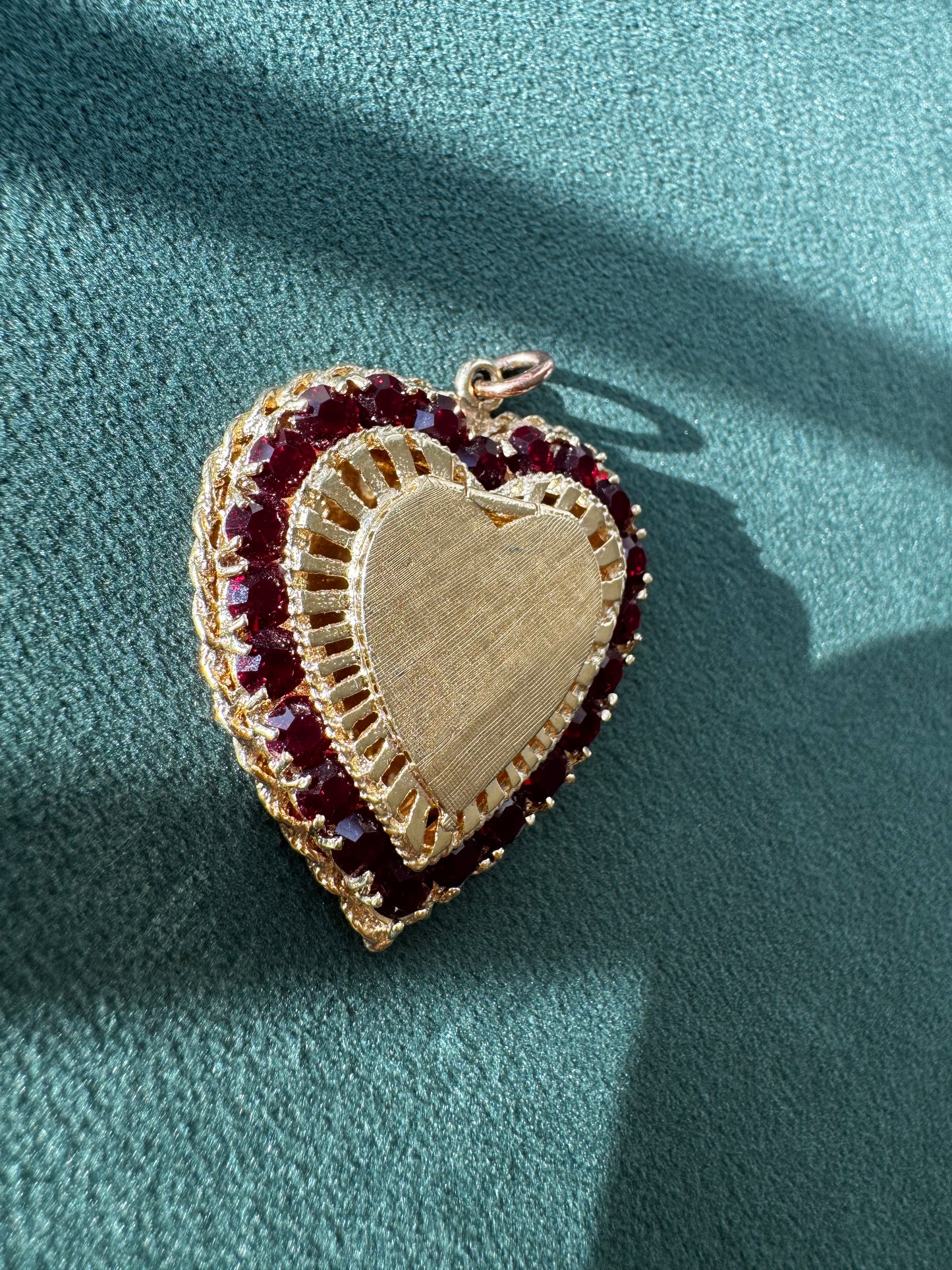 Heart-shaped gold pendant with red gemstones on a teal fabric background