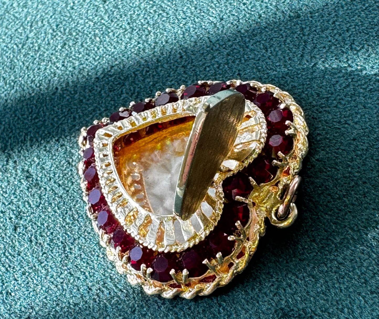 Heart-shaped gold pendant with embedded gemstones on a teal fabric background