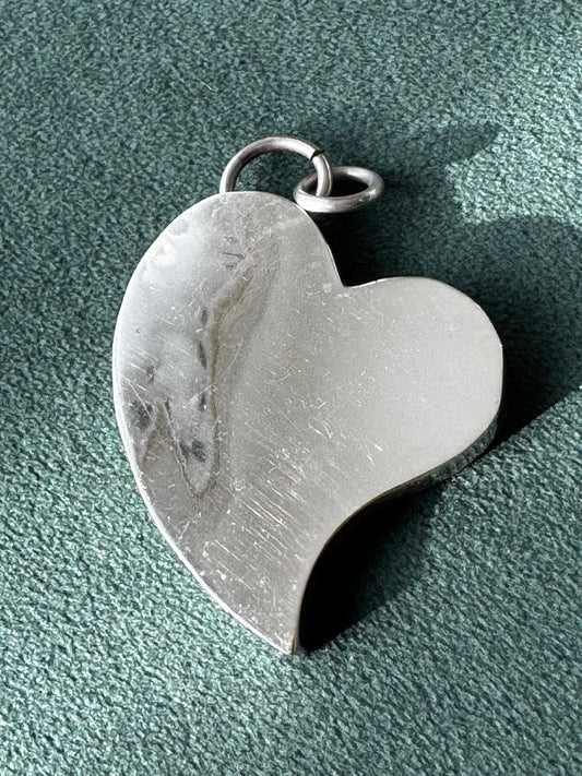 Heart-shaped silver pendant on a textured green surface