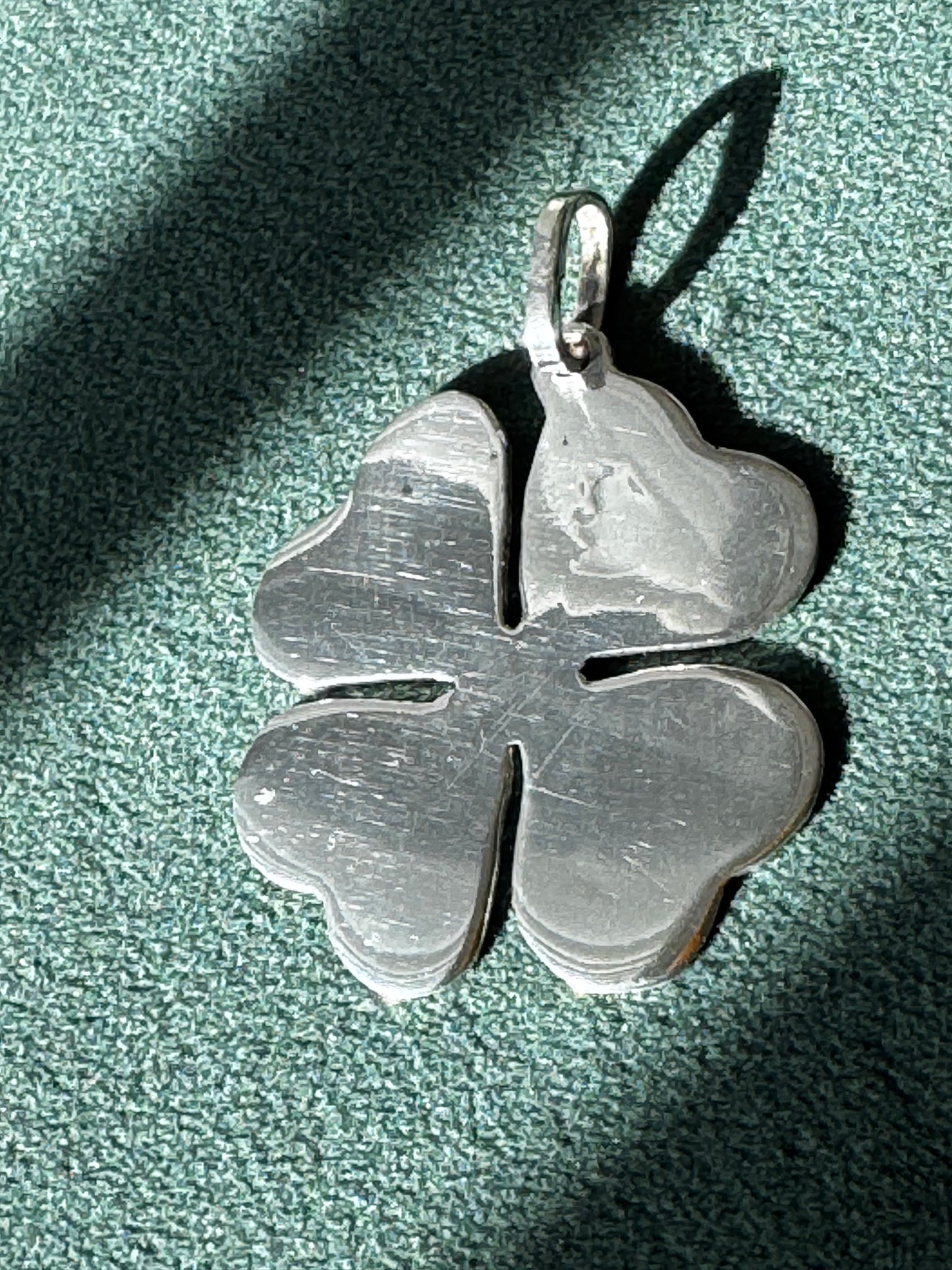 Silver four-leaf clover pendant on a textured green surface