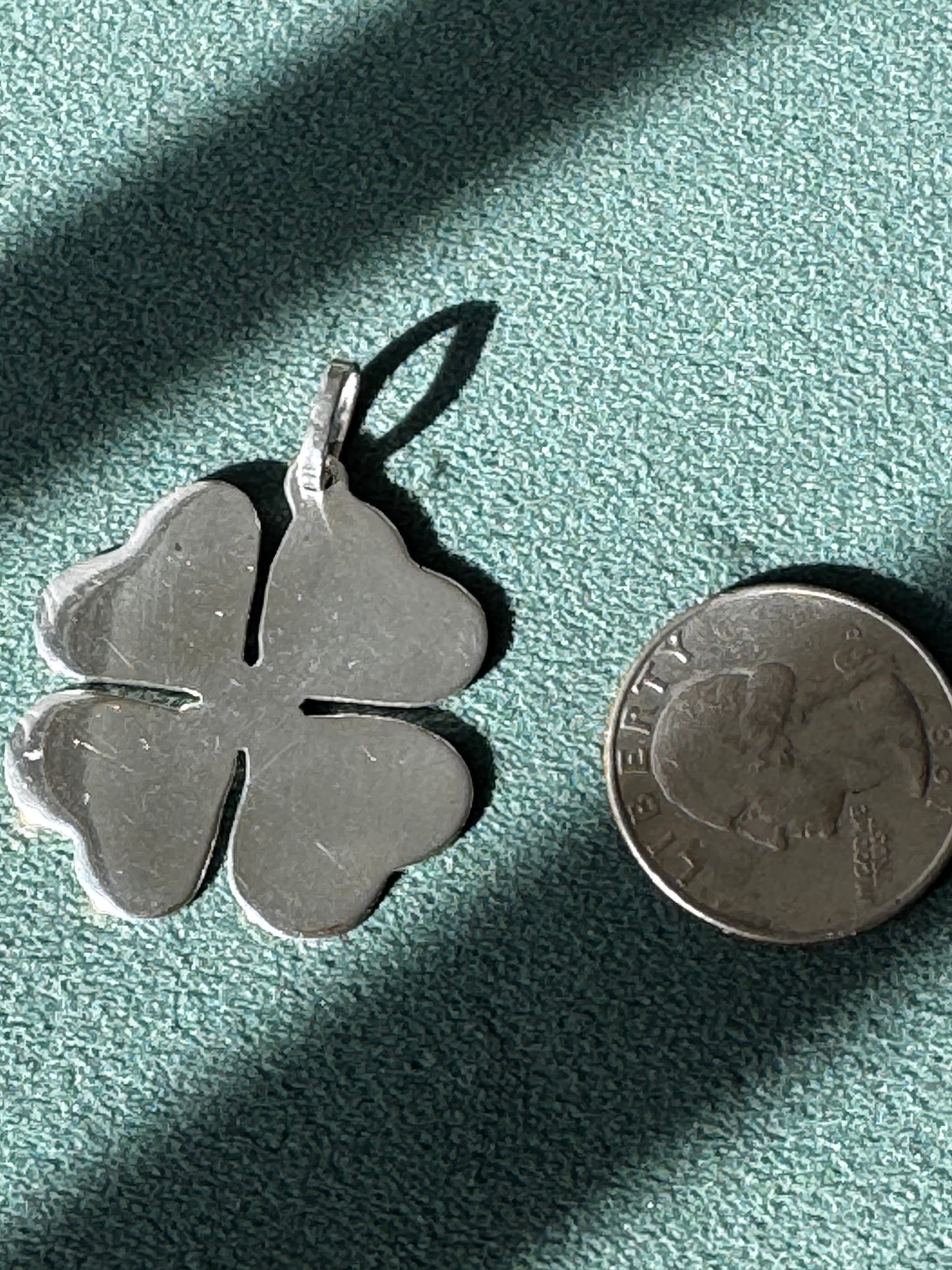 Silver four-leaf clover pendant next to a quarter on a textured green surface