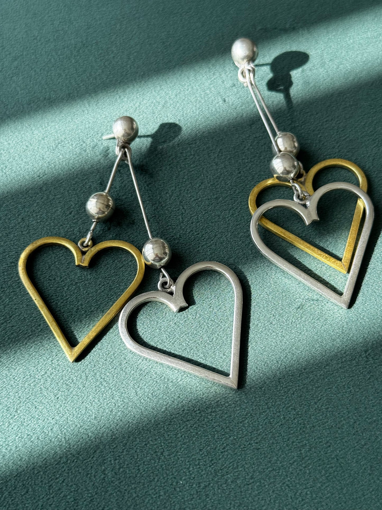 Heart-shaped earrings with gold and silver finish on a green background