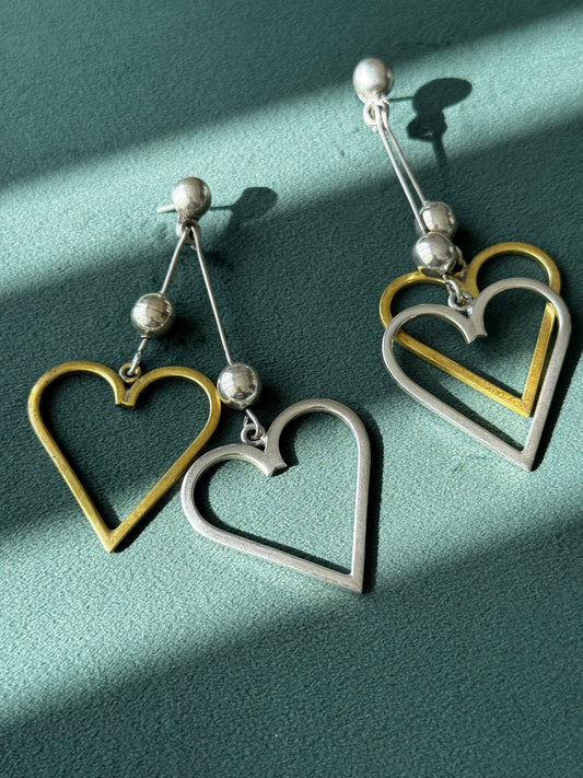 Heart-shaped earrings with gold and silver finish on a green background