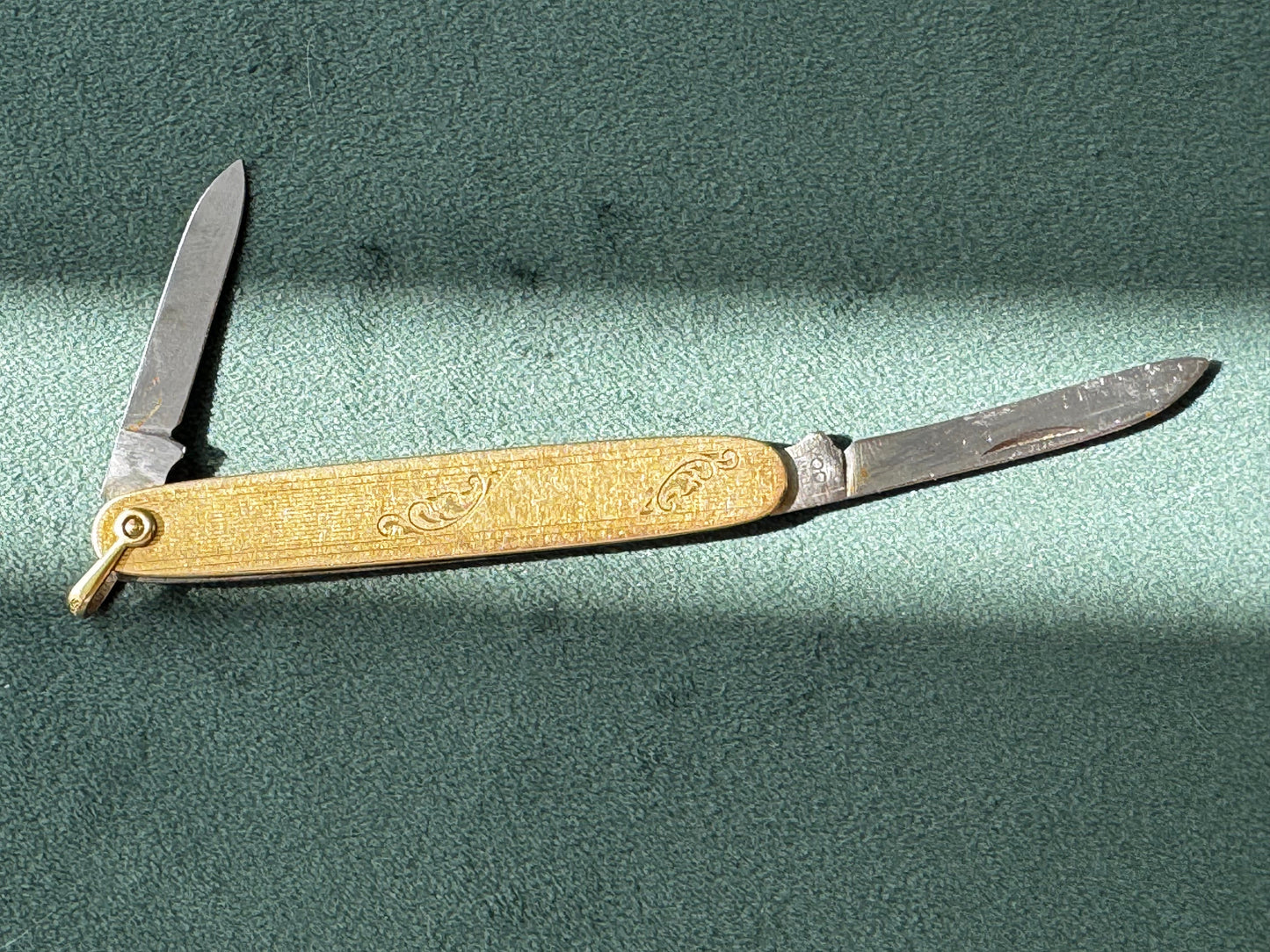 Vintage folding knife with brass blade on a green surface
