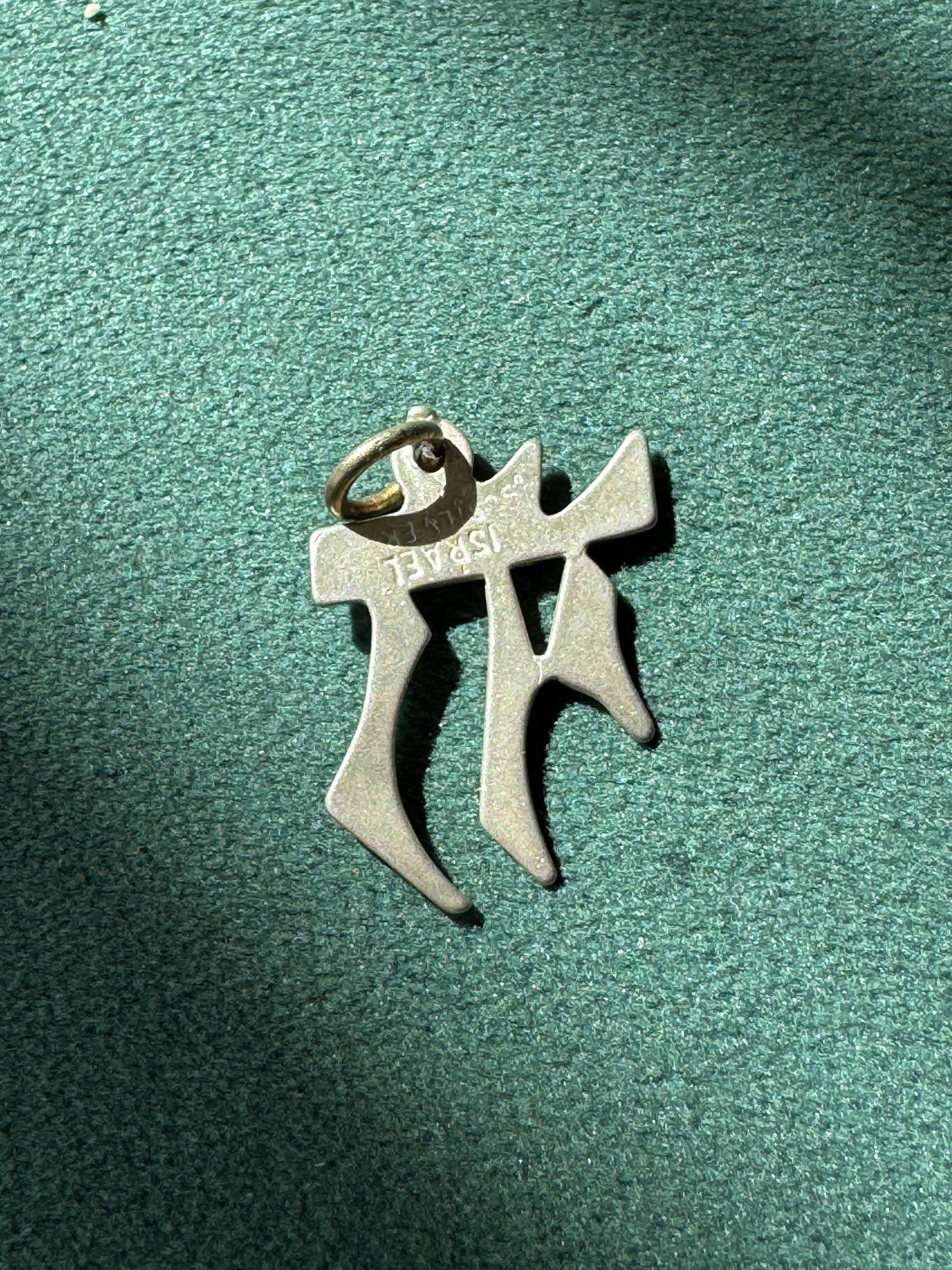 Metallic pendant with 'AMC' branding on a green textured background