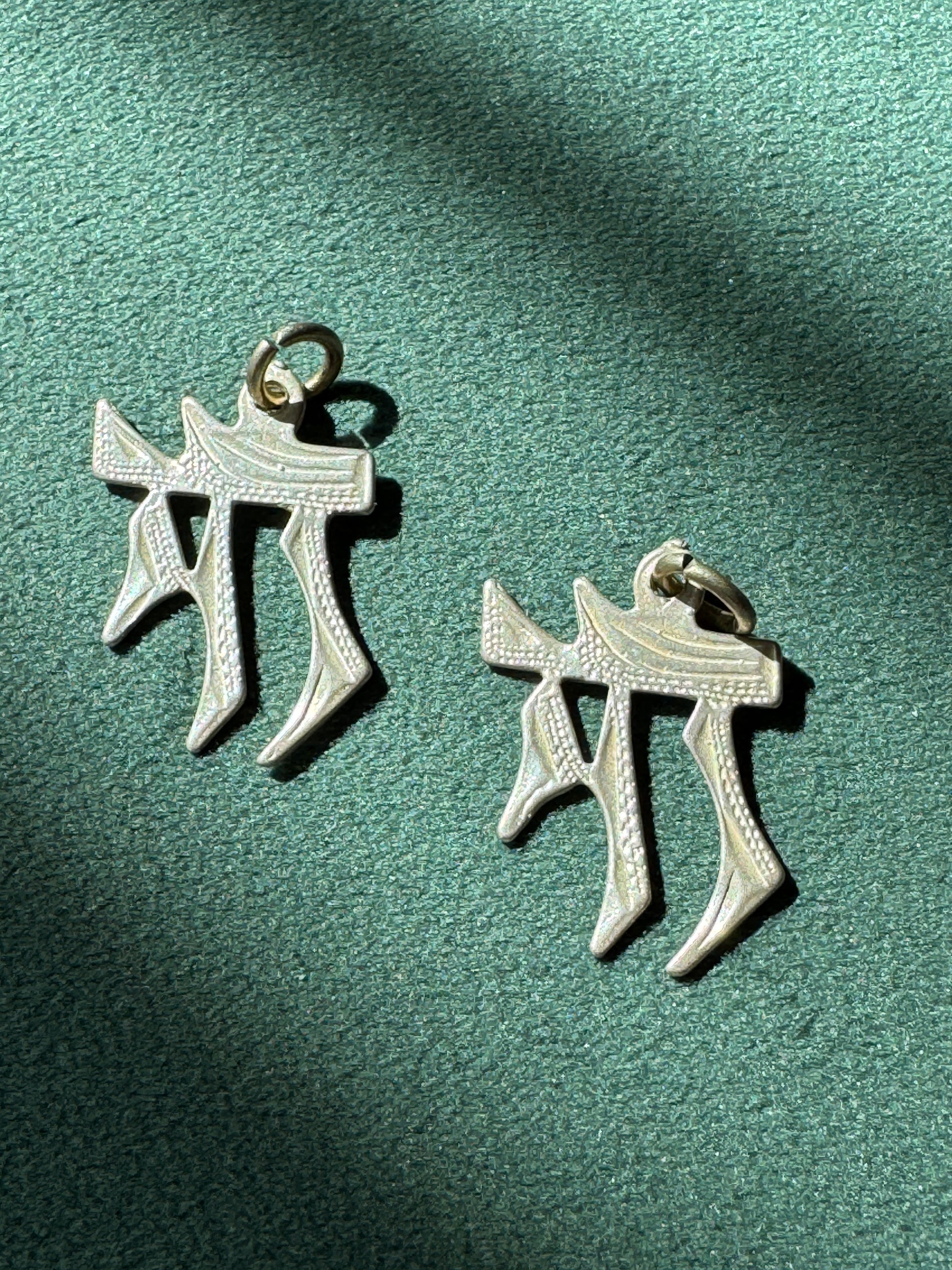 Two silver pendants on a green fabric background