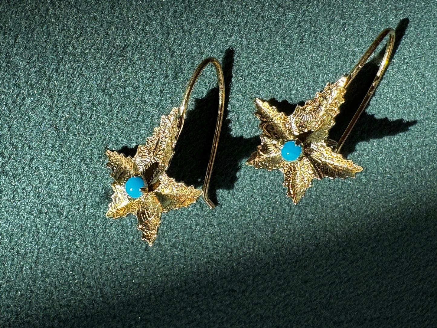 Pair of gold leaf-shaped earrings with blue centers on a green textured background
