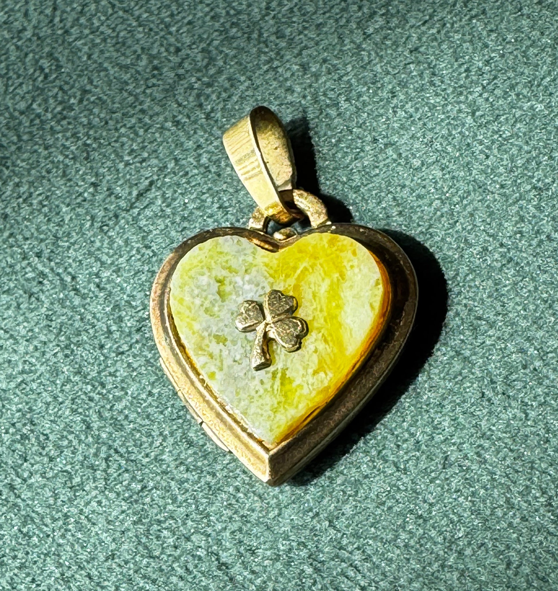 Heart-shaped pendant with clover design on a green textured surface