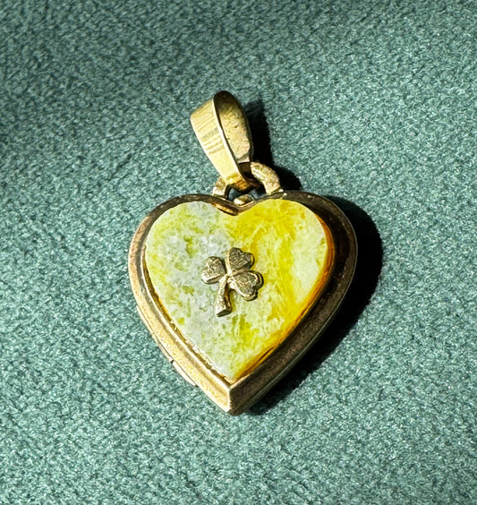 Heart-shaped pendant with clover design on a green textured surface