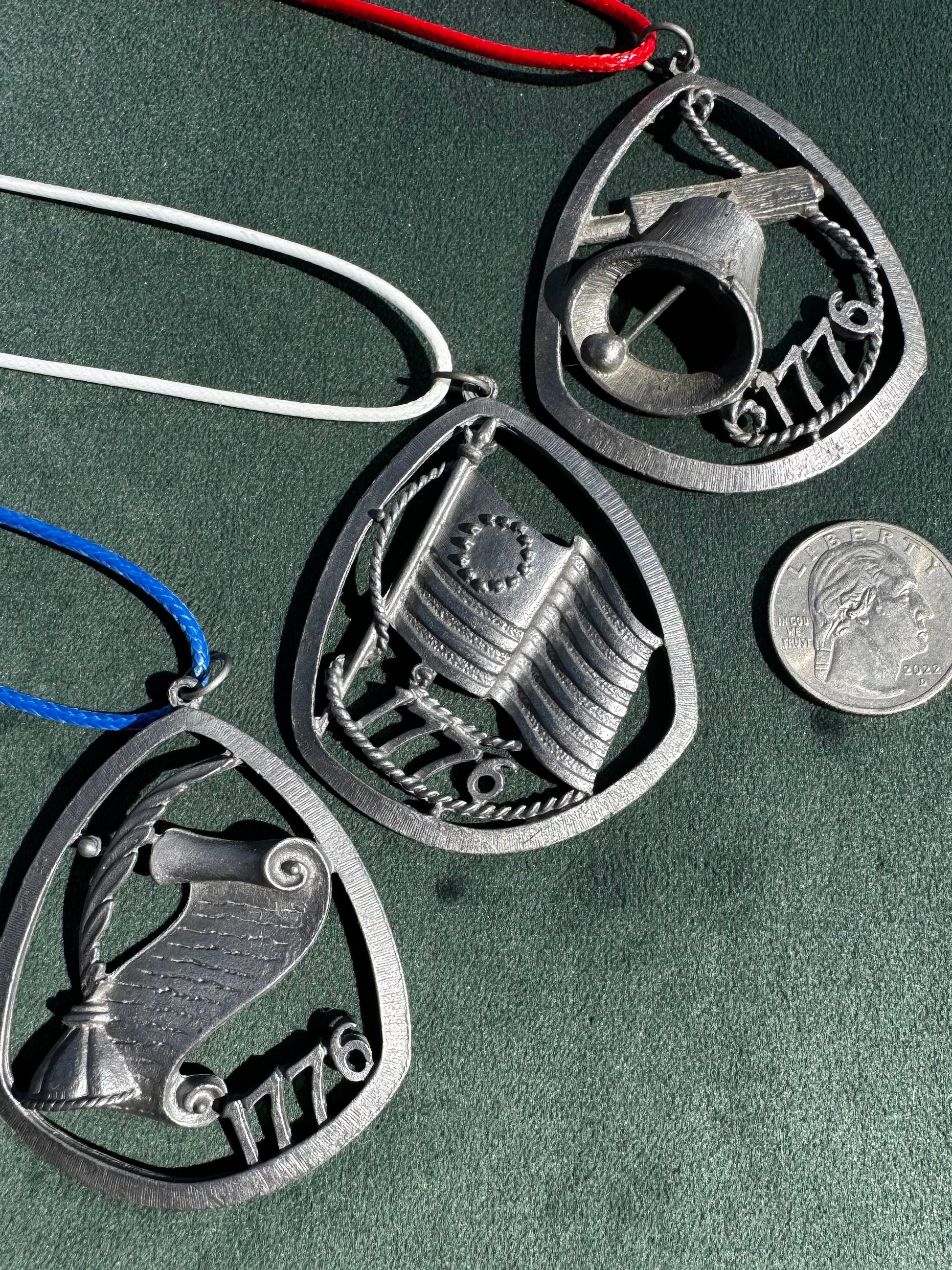 Three metallic charms with intricate designs on a green surface, one coin for scale.