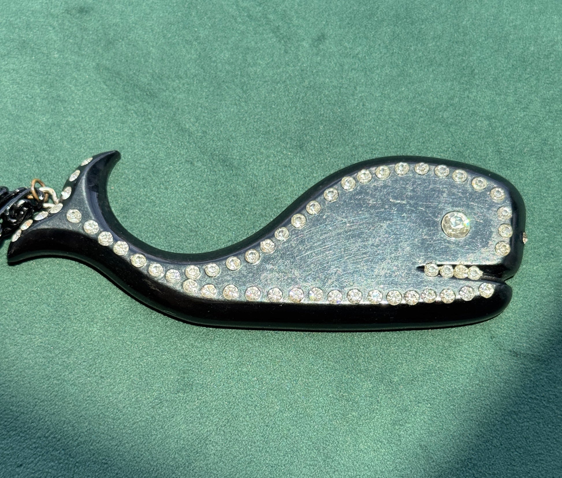 Decorative necklace shaped like a whale with rhinestones on a green background