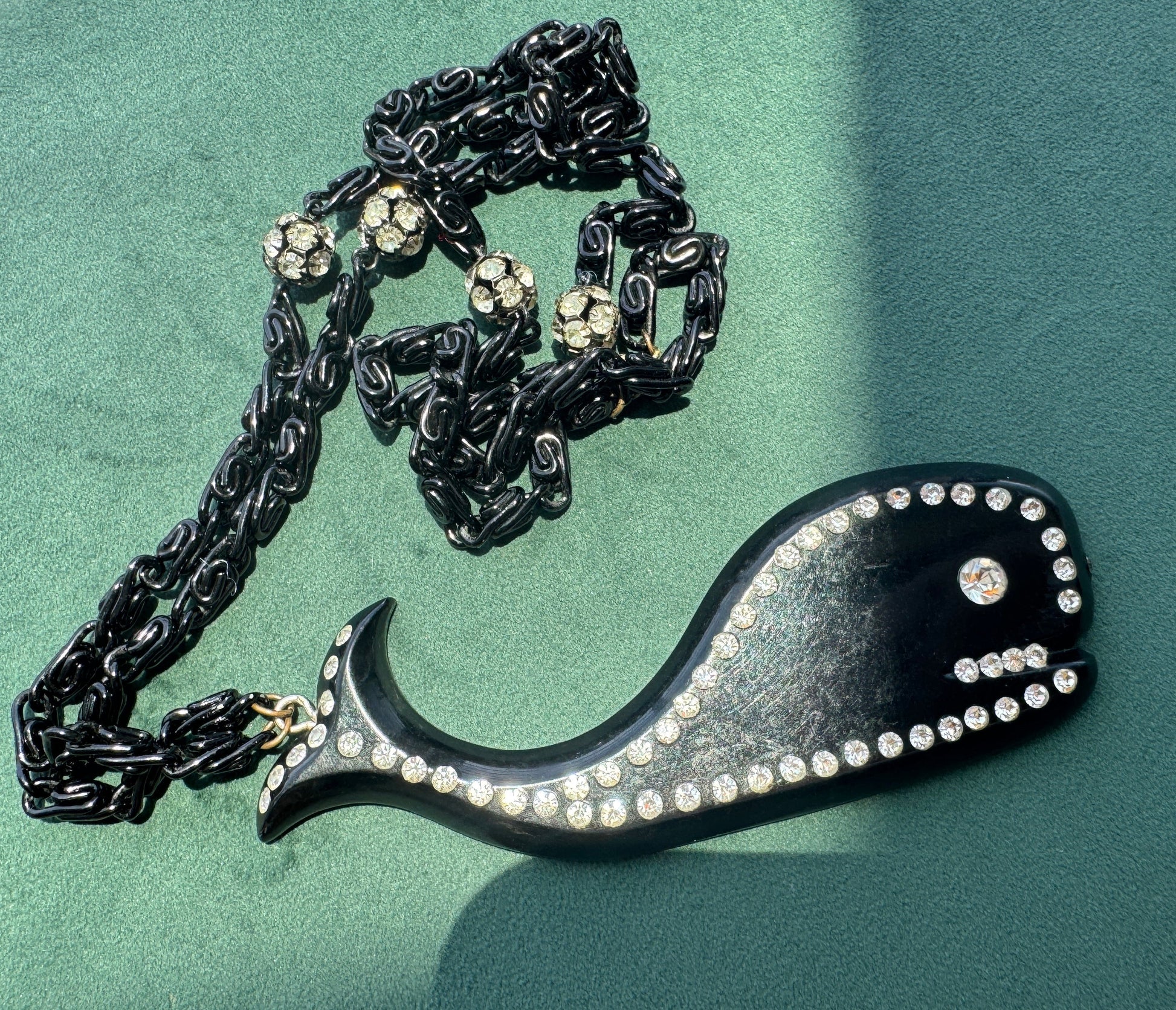 Black necklace with decorative pendant on a green surface