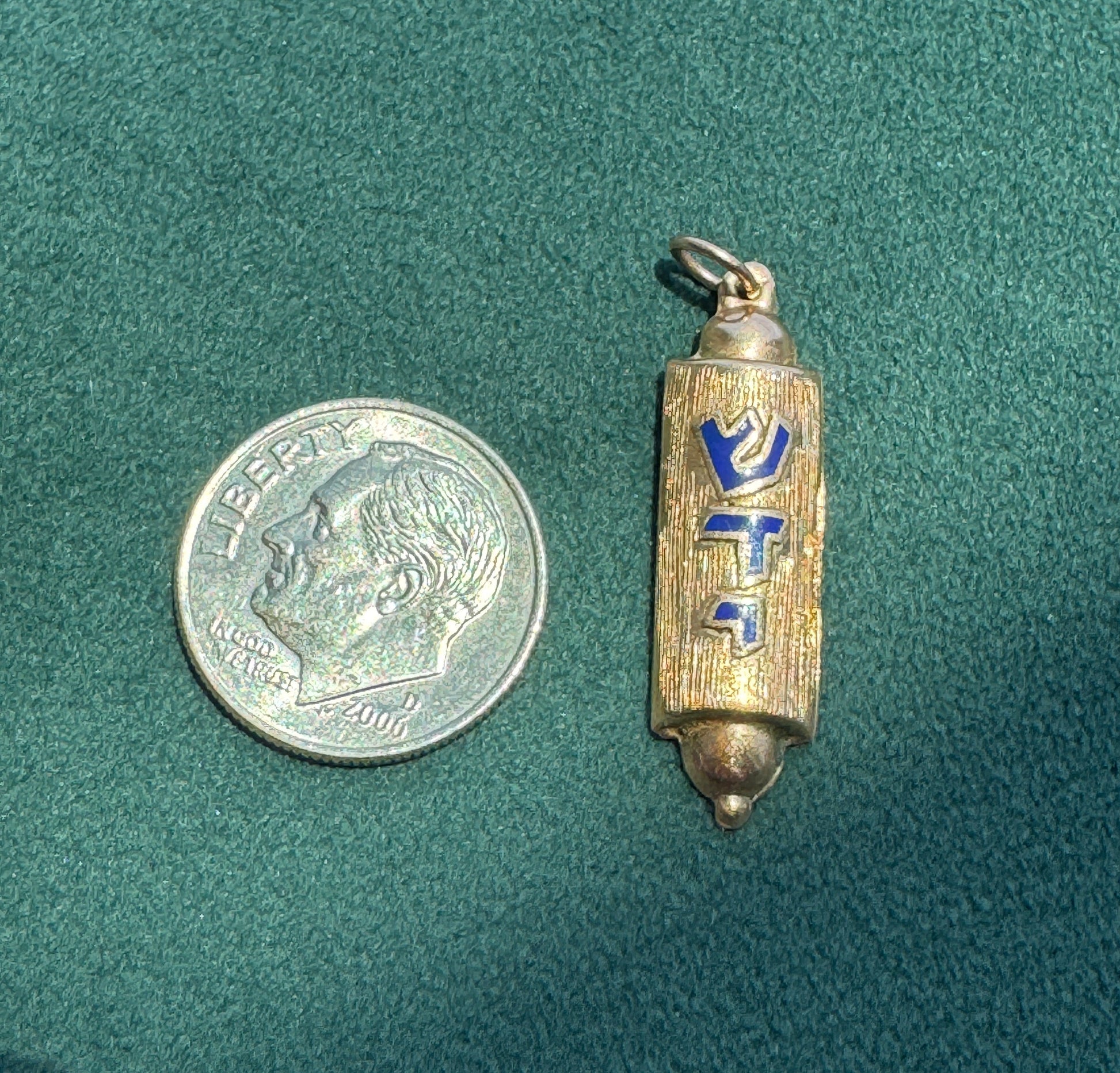 Small cylindrical metal object with blue and gold design next to a U.S. dime on a green textured surface