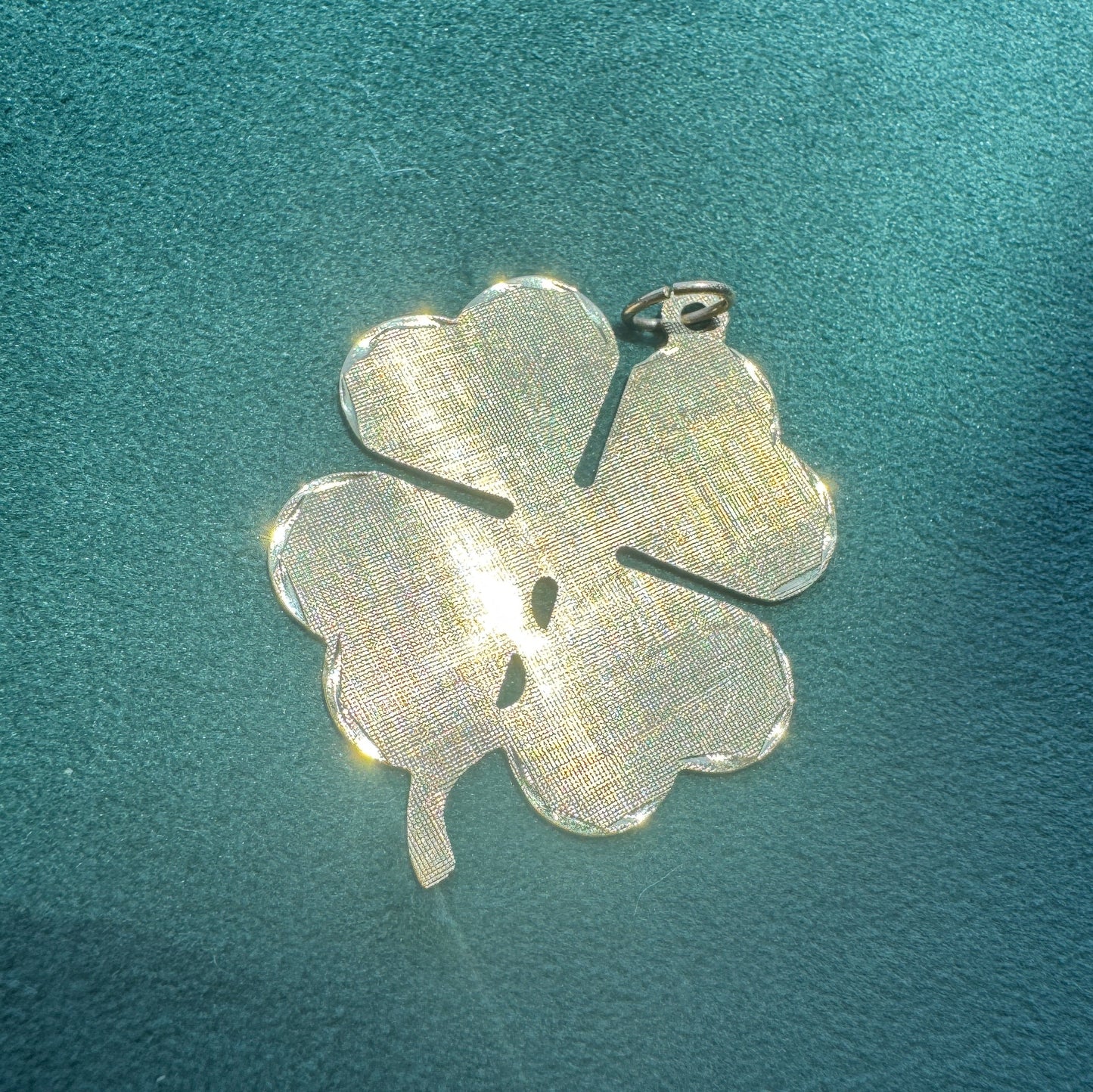 Silver four-leaf clover pendant on a textured teal background