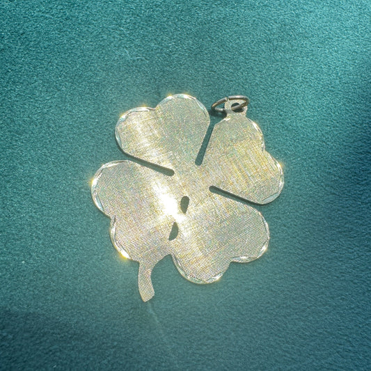 Silver four-leaf clover pendant on a textured teal background