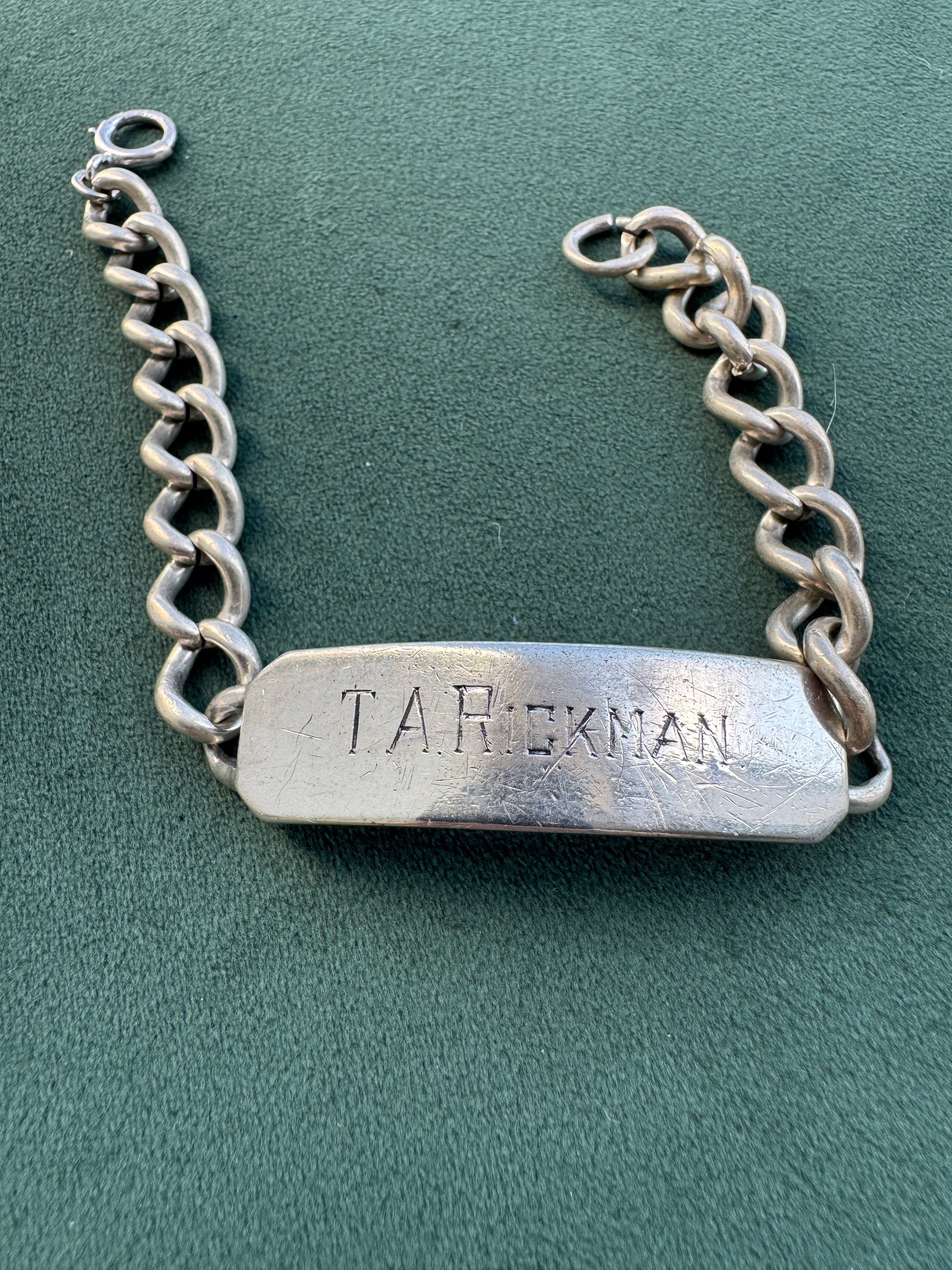 A silver-tone metal chain bracelet with a rectangular nameplate engraved with the name 'T.A.