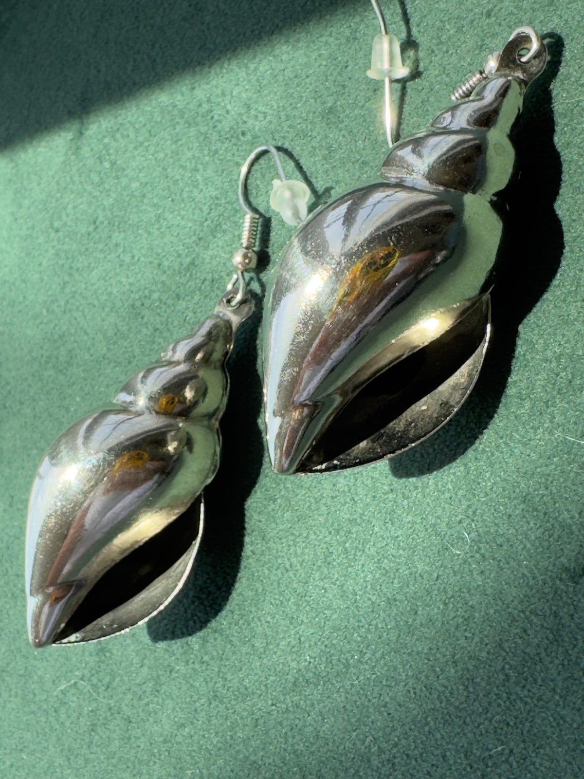 A pair of dangling shell-shaped earrings with a polished metallic finish, displayed on a textured green surface.