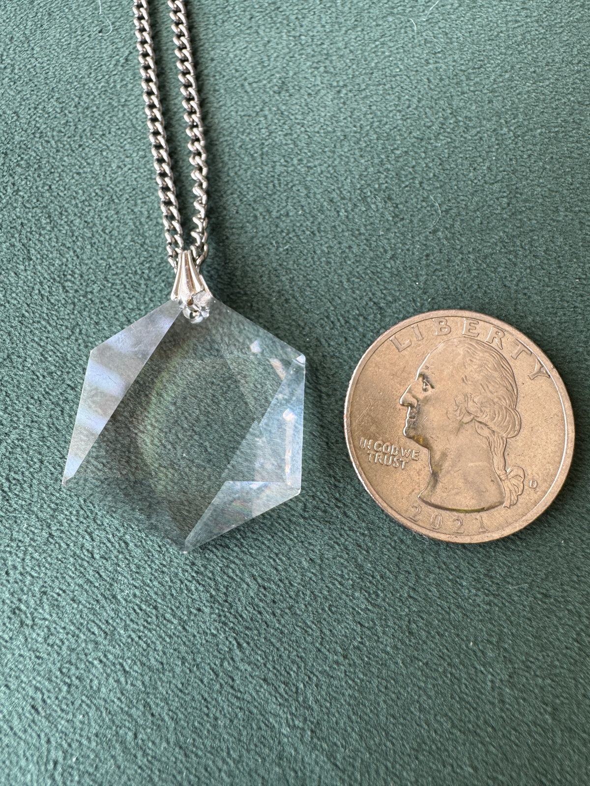 A faceted clear crystal pendant necklace on a silver chain, shown next to a U.S.